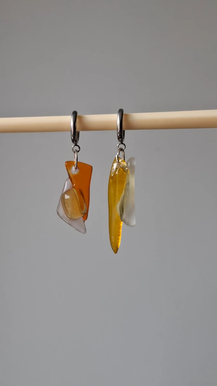 Paire de boucles d'oreilles asymétriques en verre jaune et orange suspendues sur un support en bois