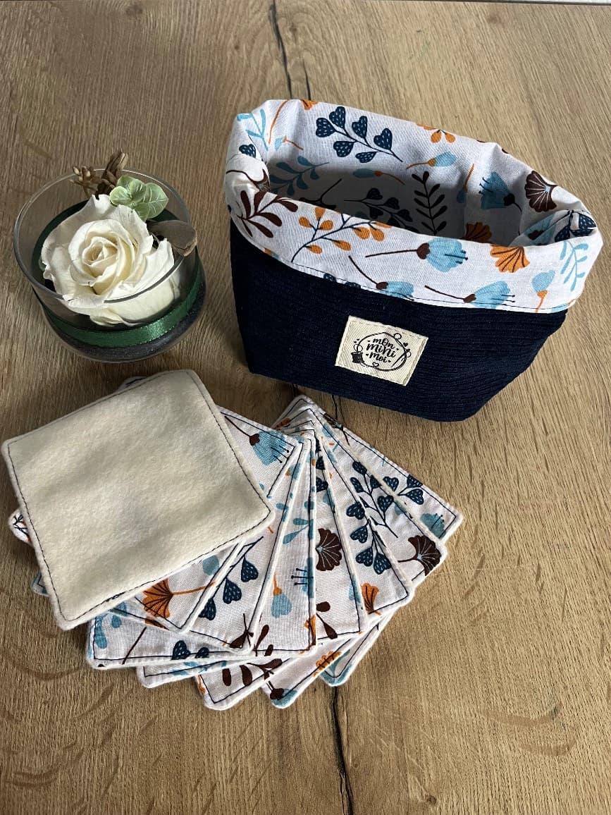 Panier en tissu côtelé bleu marine et lingettes lavables à motifs floraux étalées devant.