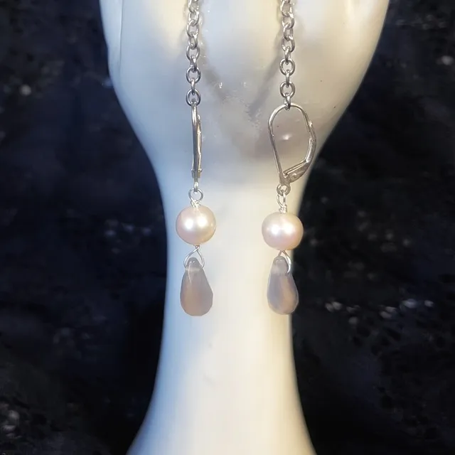 Gros plan sur les dormeuses Arista en argent, ornées d'une perle blanche et d'une agate taillée en goutte.
