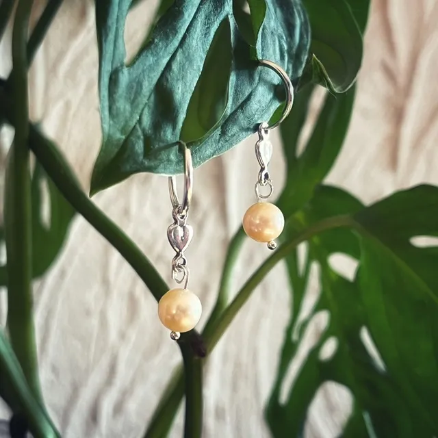 Créoles en argent ornées d'un motif cœur et d'une perle d'eau douce, suspendues à une feuille verte.