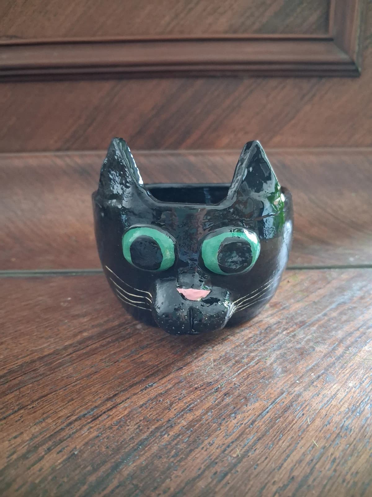 Pot en céramique noire en forme de tête de chat aux yeux verts et nez rose sur fond en bois