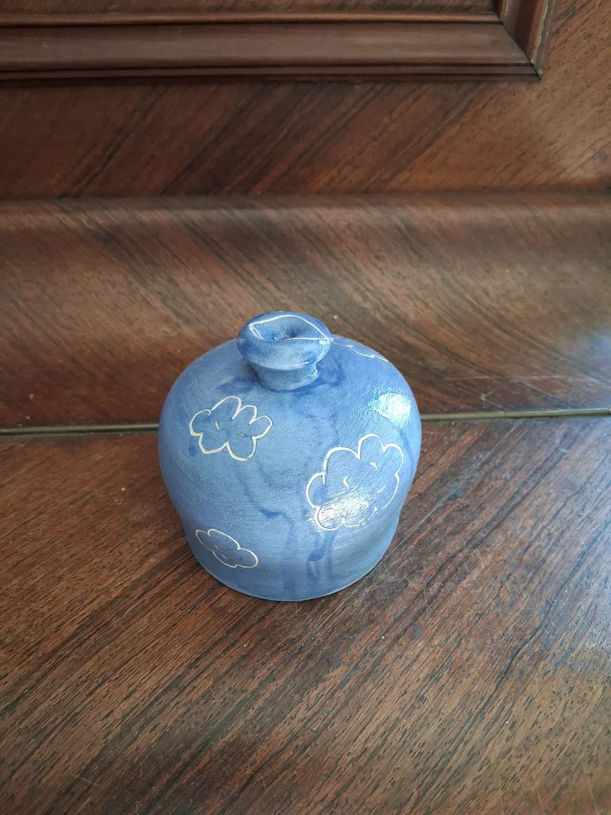 Arrosoir-main sphérique en céramique bleue décoré de motifs de nuages, posé sur un fond en bois.