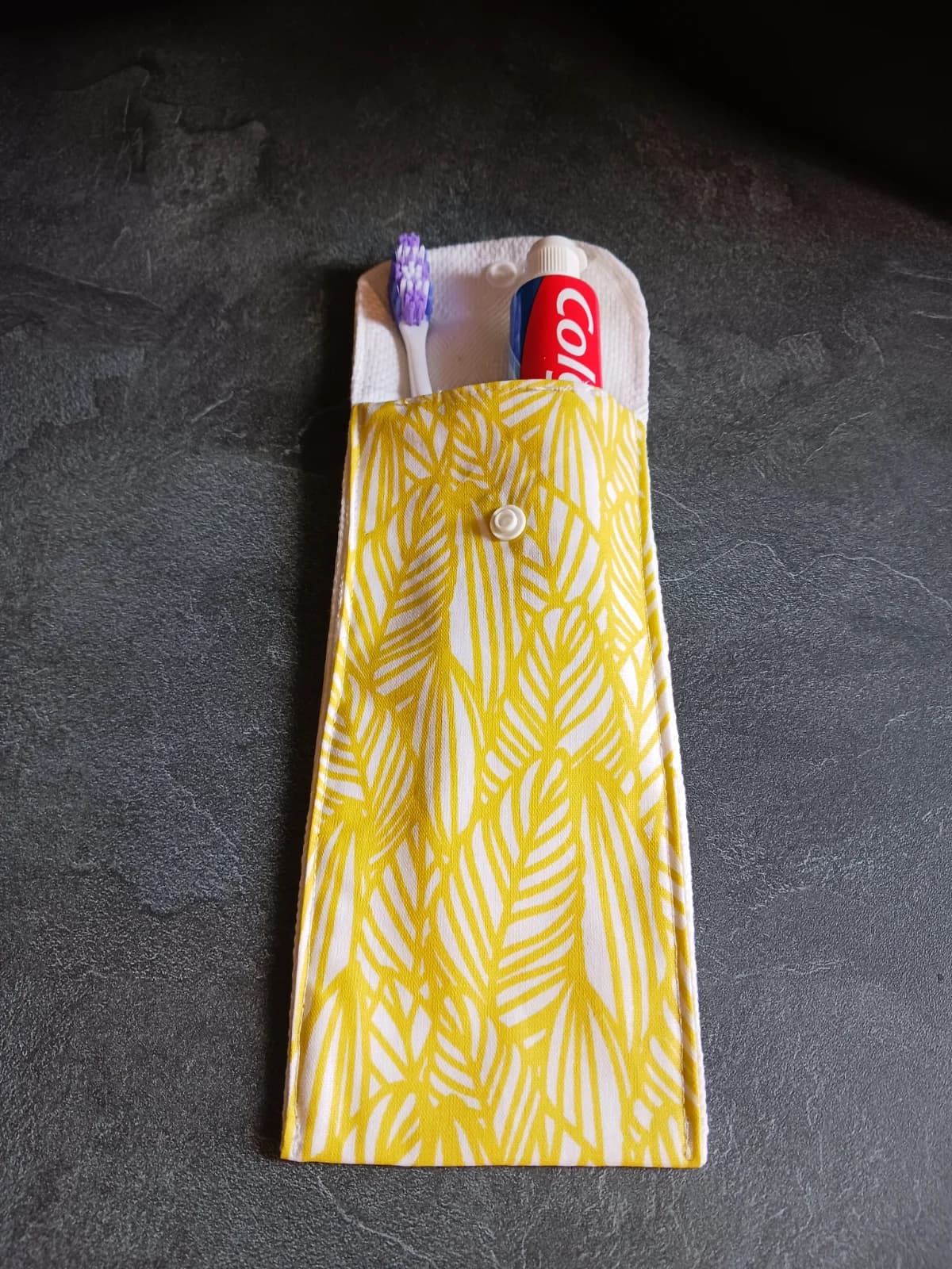 Étui en tissu ouvert à motif de feuilles jaunes contenant une brosse à dents et un dentifrice.