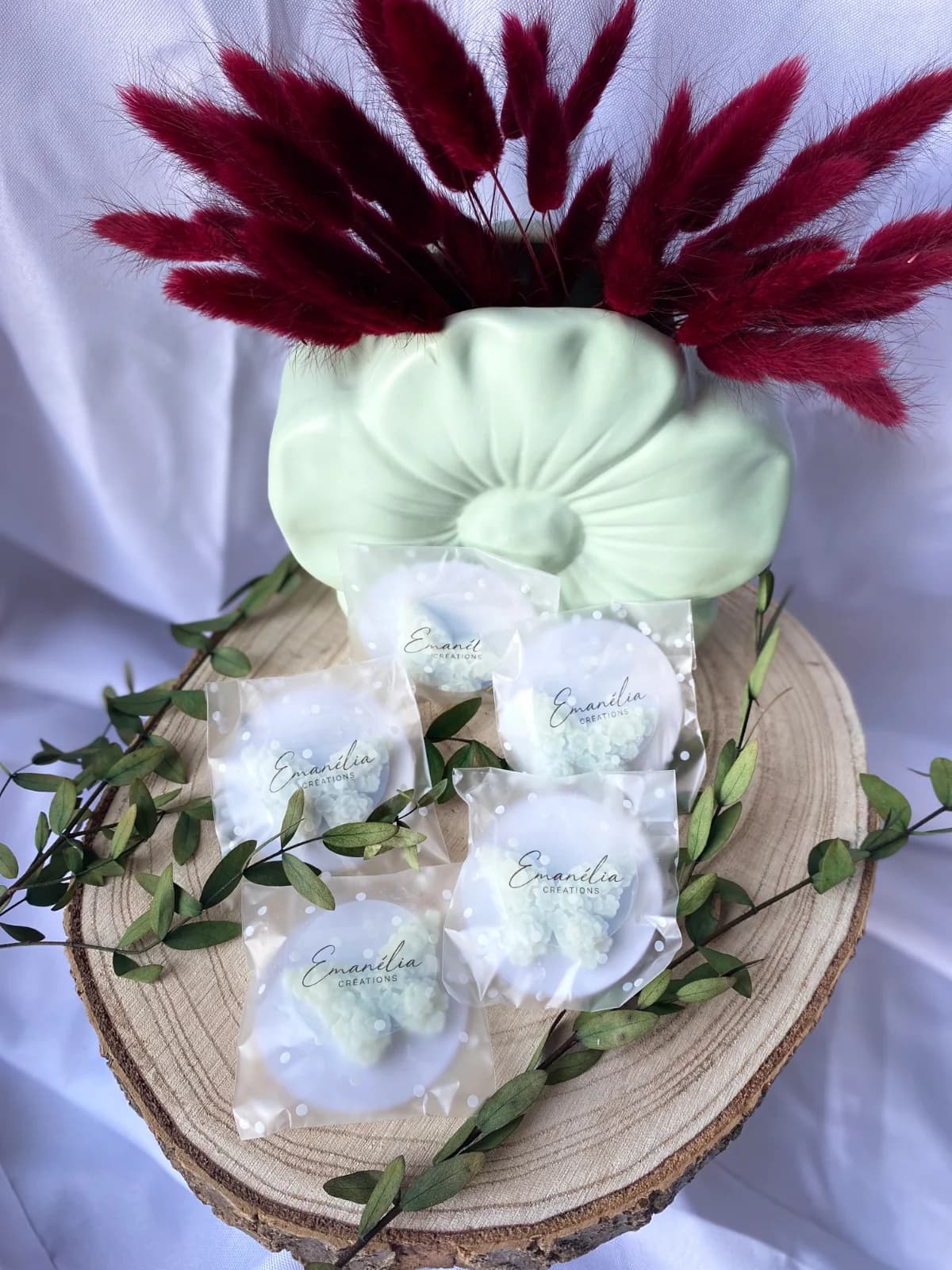 Fondants parfumés papillons sous sachets posés sur un rondin de bois près d'un vase et de fleurs séchées.