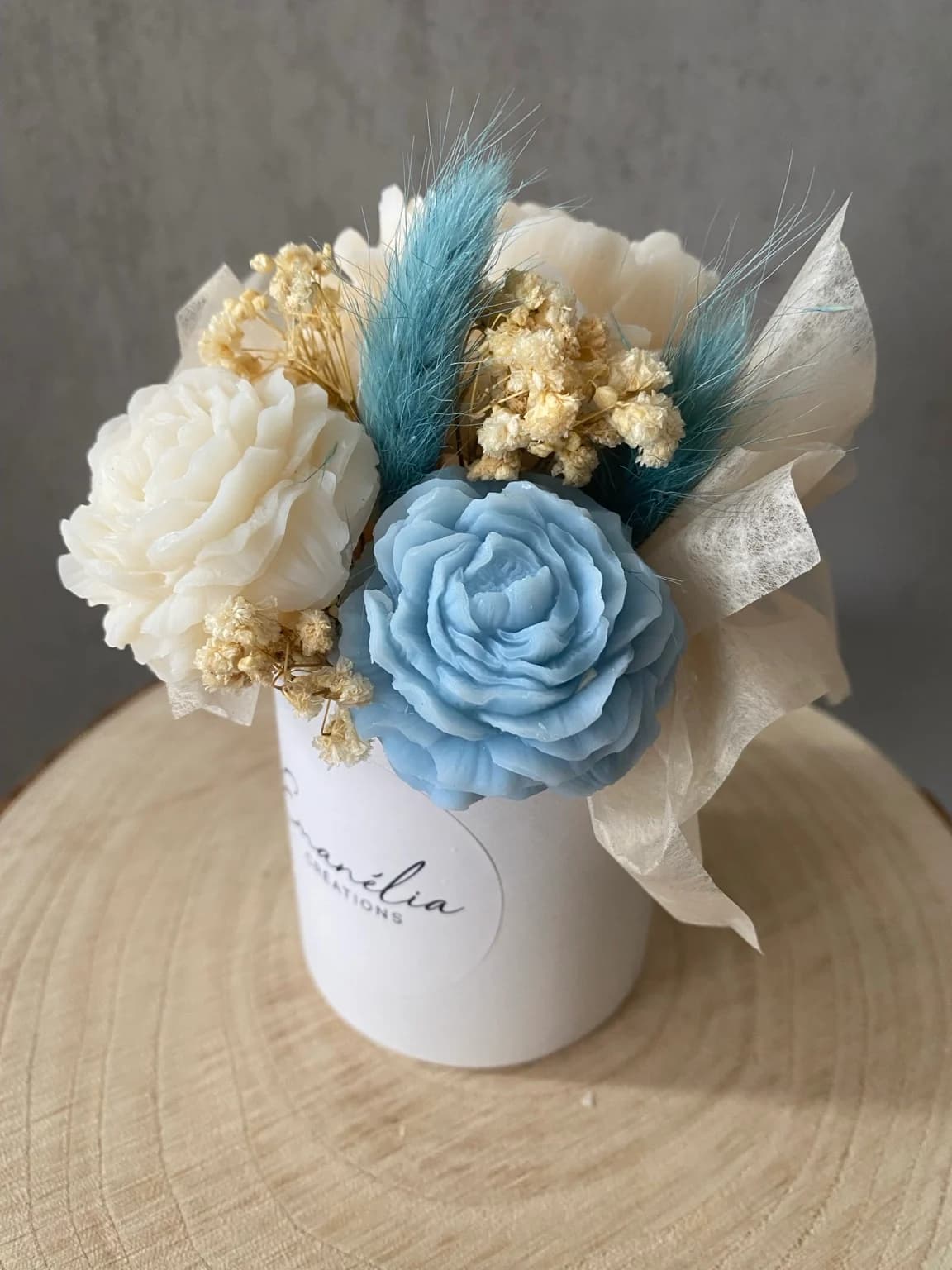 Gros plan sur les fleurs sculptées en cire blanche et bleue accompagnées de petites fleurs séchées.